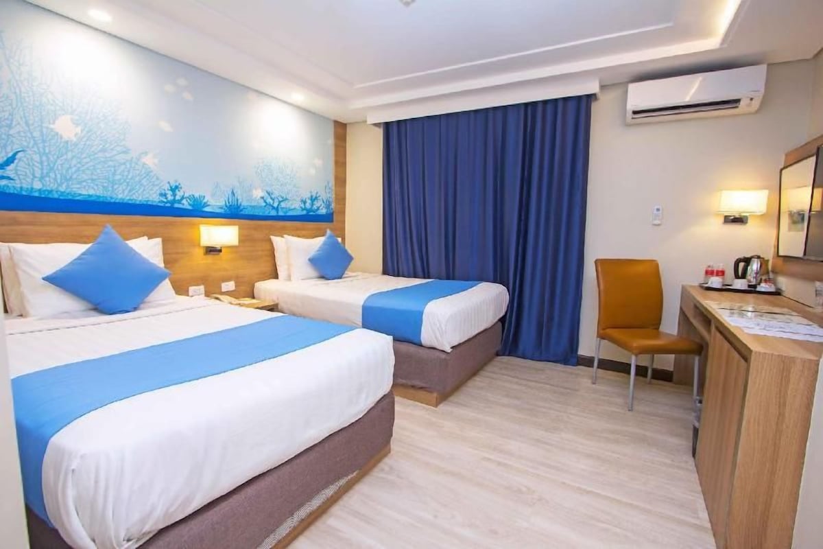 A hotel room with two beds, a desk, a chair, an air conditioner, and a wall mural.