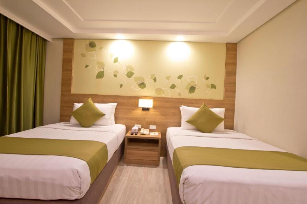 A hotel room with two beds, a nightstand, a wall-mounted lamp, and a decorative leaf pattern on the wall.