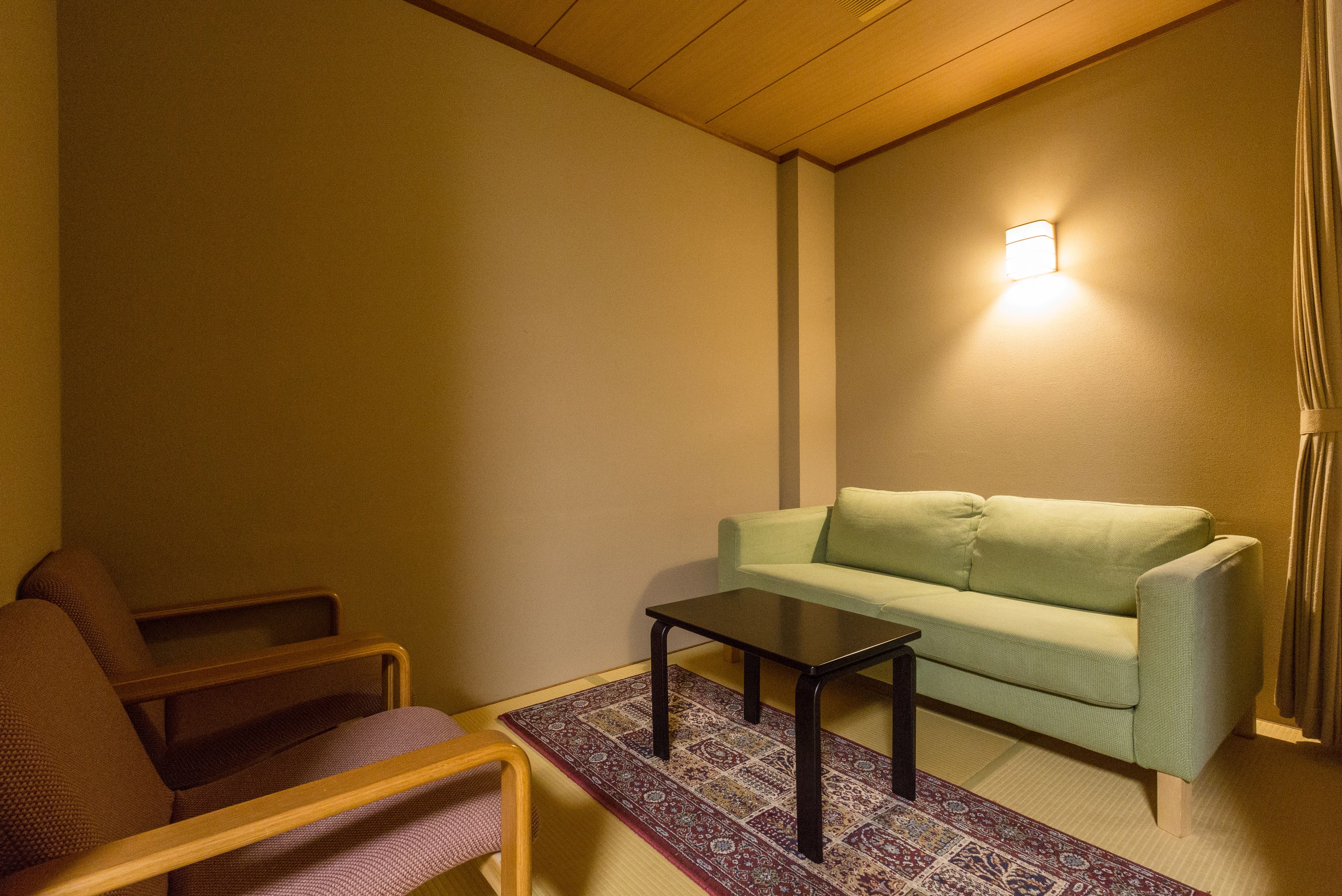 Ein Zimmer mit einem grünen Sofa, einem Holzstuhl, einem kleinen Tisch und einem gemusterten Teppich.