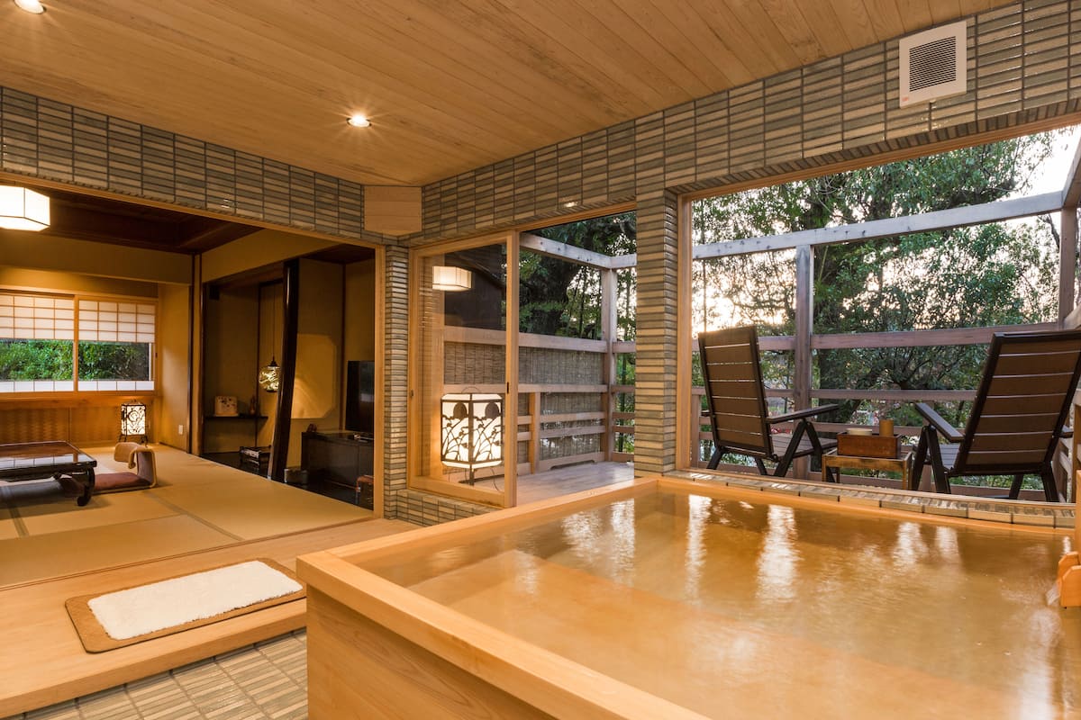 A traditional Japanese onsen with tatami mats, wooden furniture, and a view of the surrounding forest.