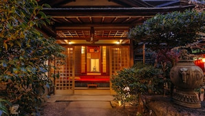 Un edificio japonés tradicional con estructura de madera, un banco rojo y una fuente de agua de piedra.