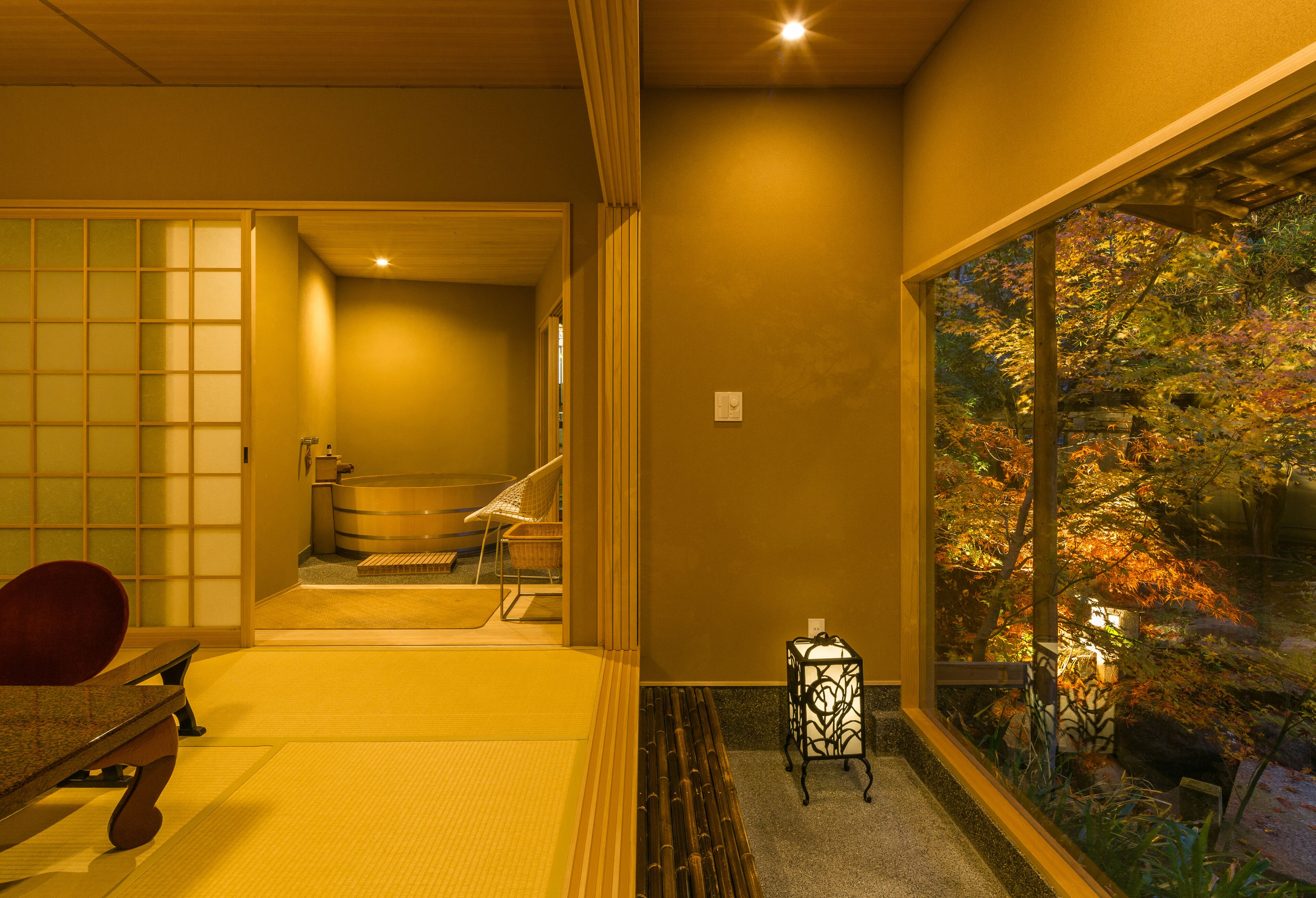 A traditional Japanese room with tatami flooring, a low table, and a view of a garden through a large window.