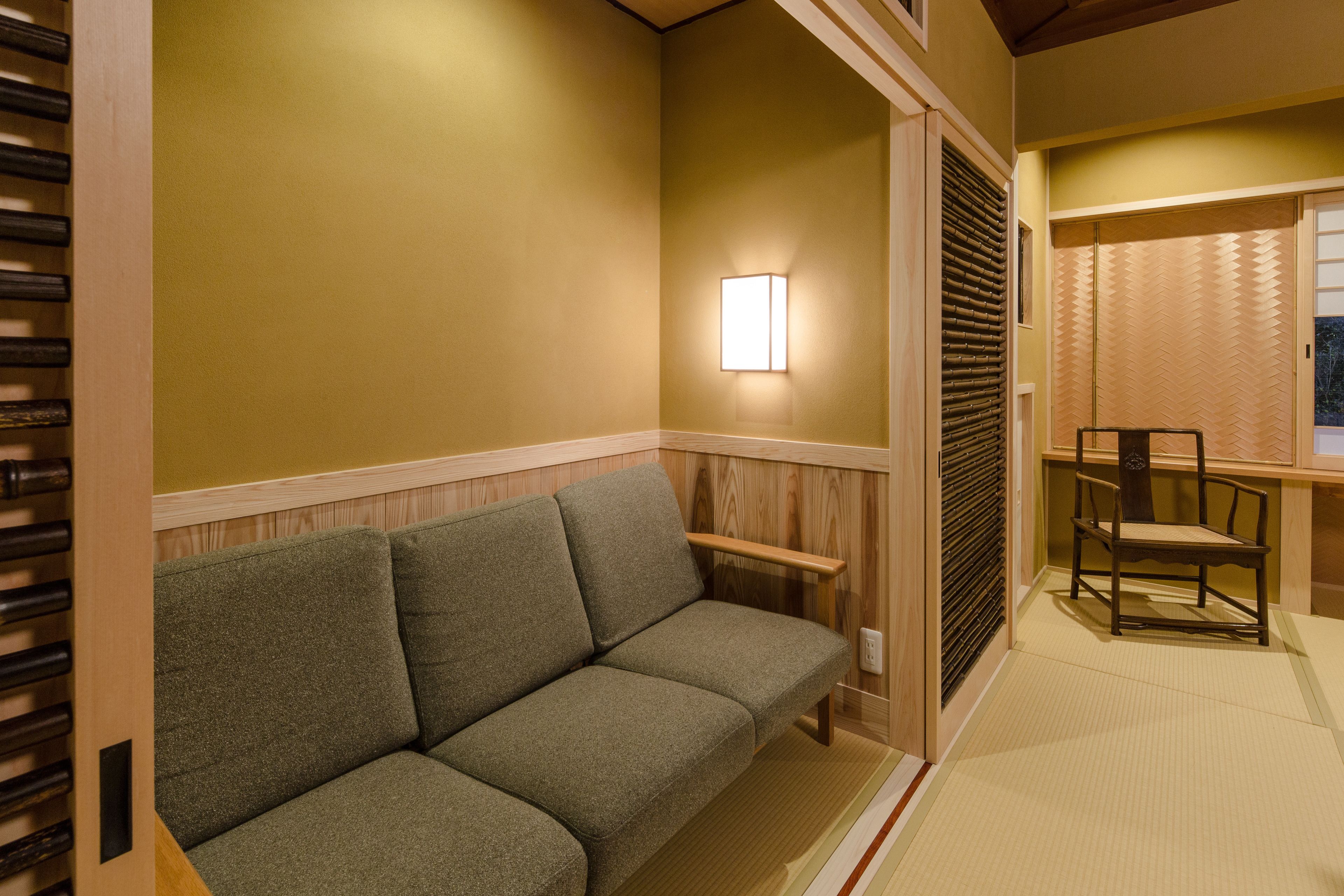 A traditional Japanese interior with a wooden sliding door, a tatami mat floor, a low green sofa, and a wooden chair.