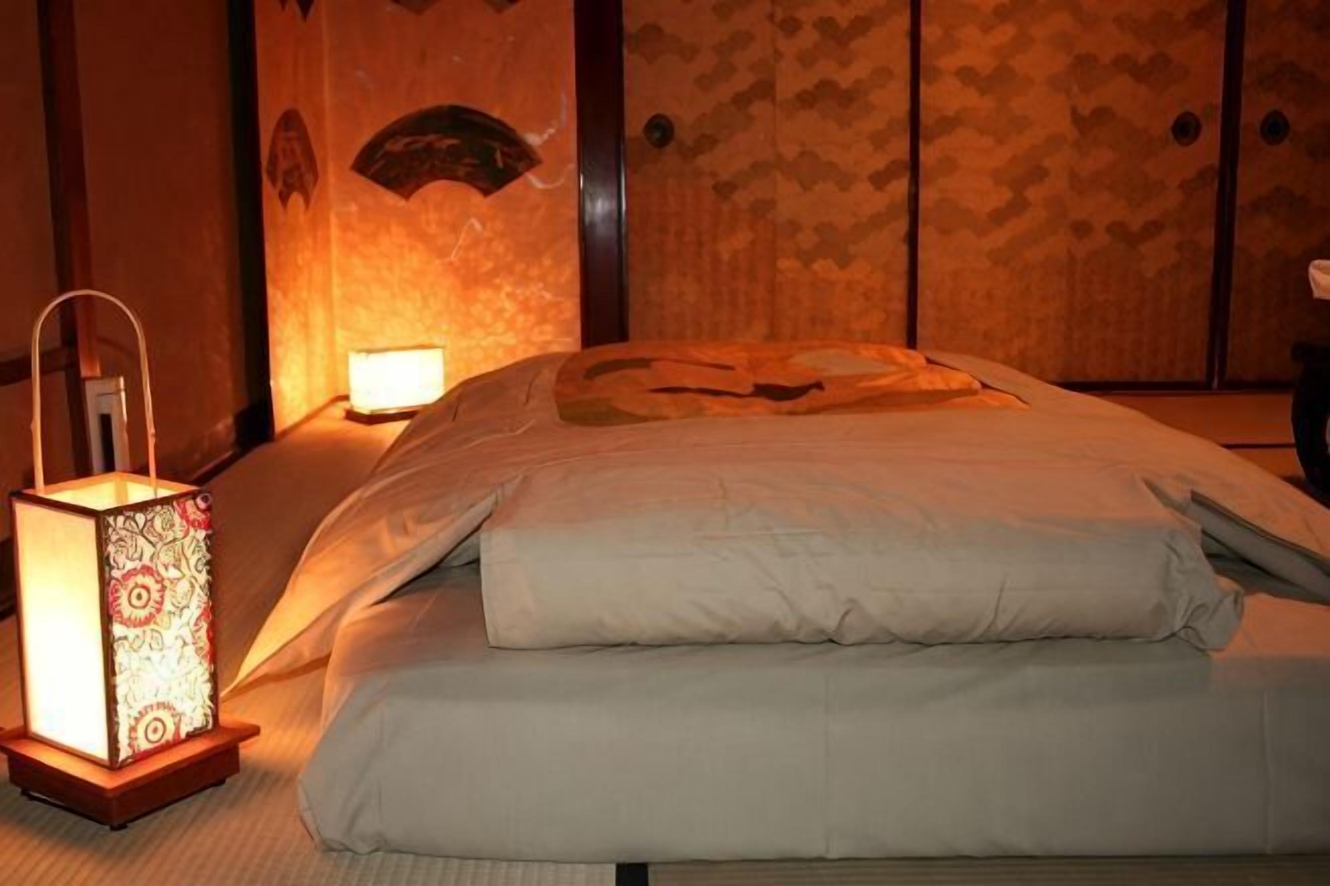 Un letto rifatto con un copriletto bianco e cuscini, un comodino con una lampada e una parete decorata.