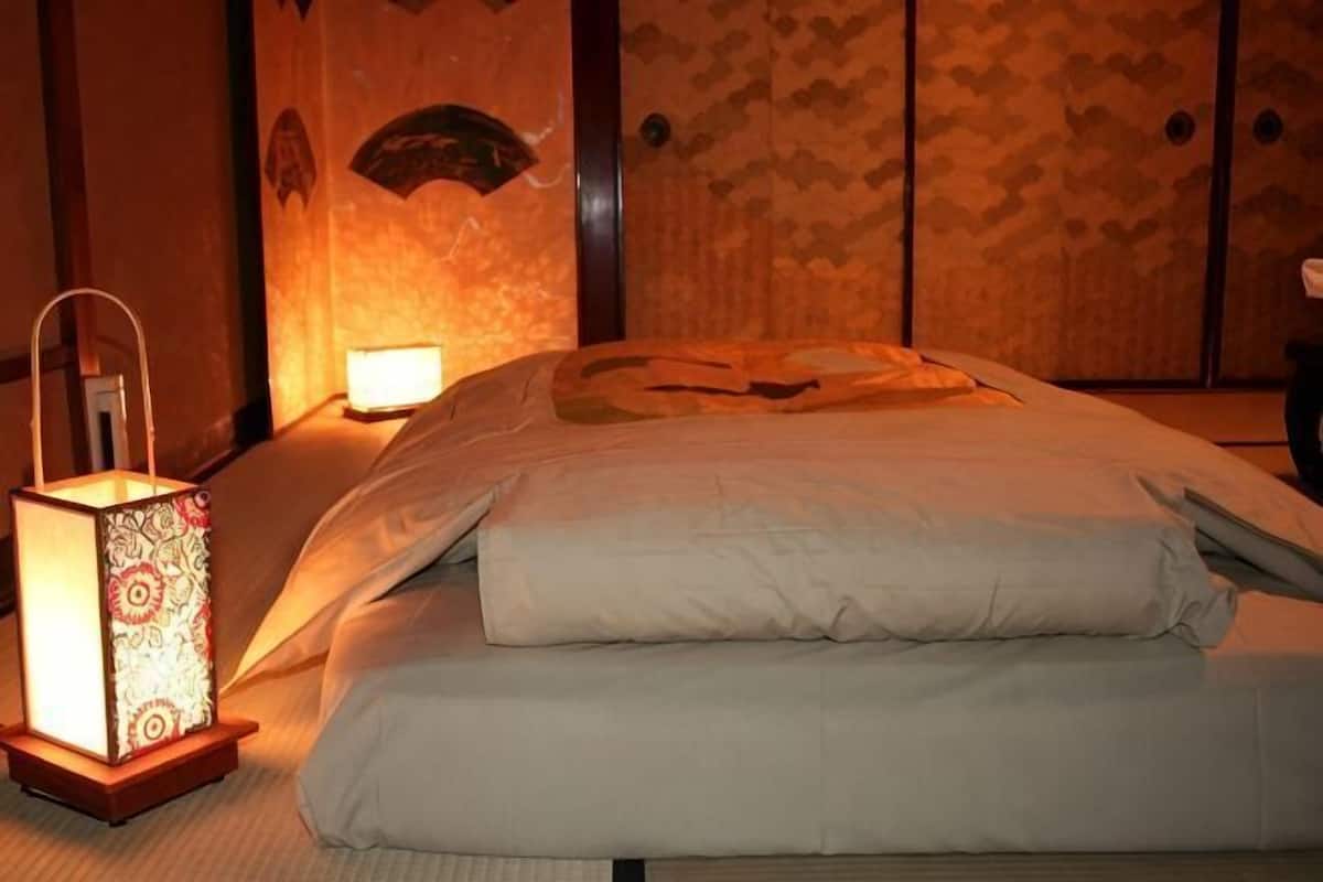A neatly made bed with a white comforter and pillows, a bedside table with a lamp, and a patterned wall.