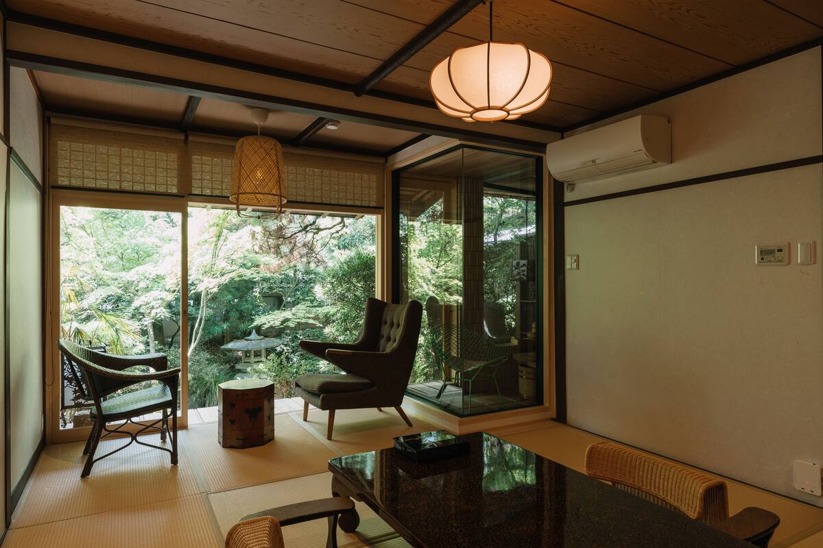 A traditional Japanese-style room with tatami flooring, a low table, and a view of lush greenery outside.