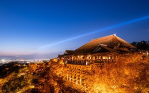 A traditional Japanese building with a thatched roof, surrounded by trees and overlooking a cityscape.