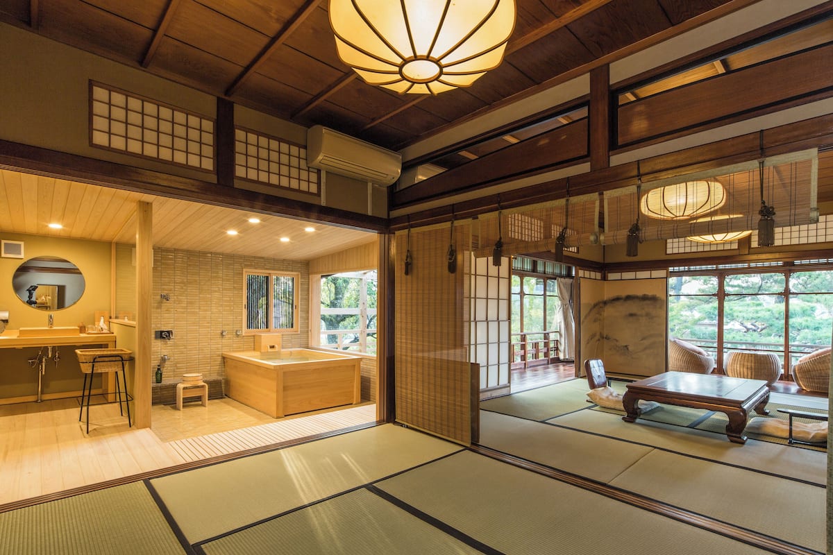 A traditional Japanese-style room with tatami flooring, a wooden desk, and a view of the garden through the sliding doors.