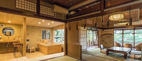 A traditional Japanese-style room with tatami flooring, a wooden desk, and a view of the garden through the sliding doors.