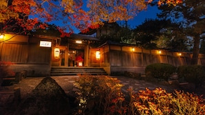 Um edifício japonês tradicional com fachada de madeira, uma placa e uma entrada bem iluminada.