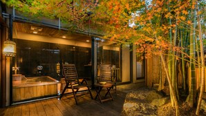 Um spa moderno com um deck de madeira, duas cadeiras de madeira, uma banheira de hidromassagem e plantas de bambu.