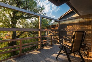 Una terraza de madera con baranda de madera, una silla de madera y vistas a árboles y un edificio al fondo.