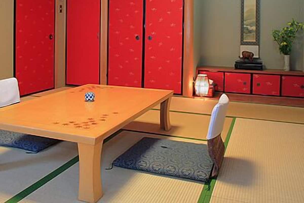 Una habitación con esterillas de tatami, una mesa baja, taquillas rojas y un pequeño armario con una planta.