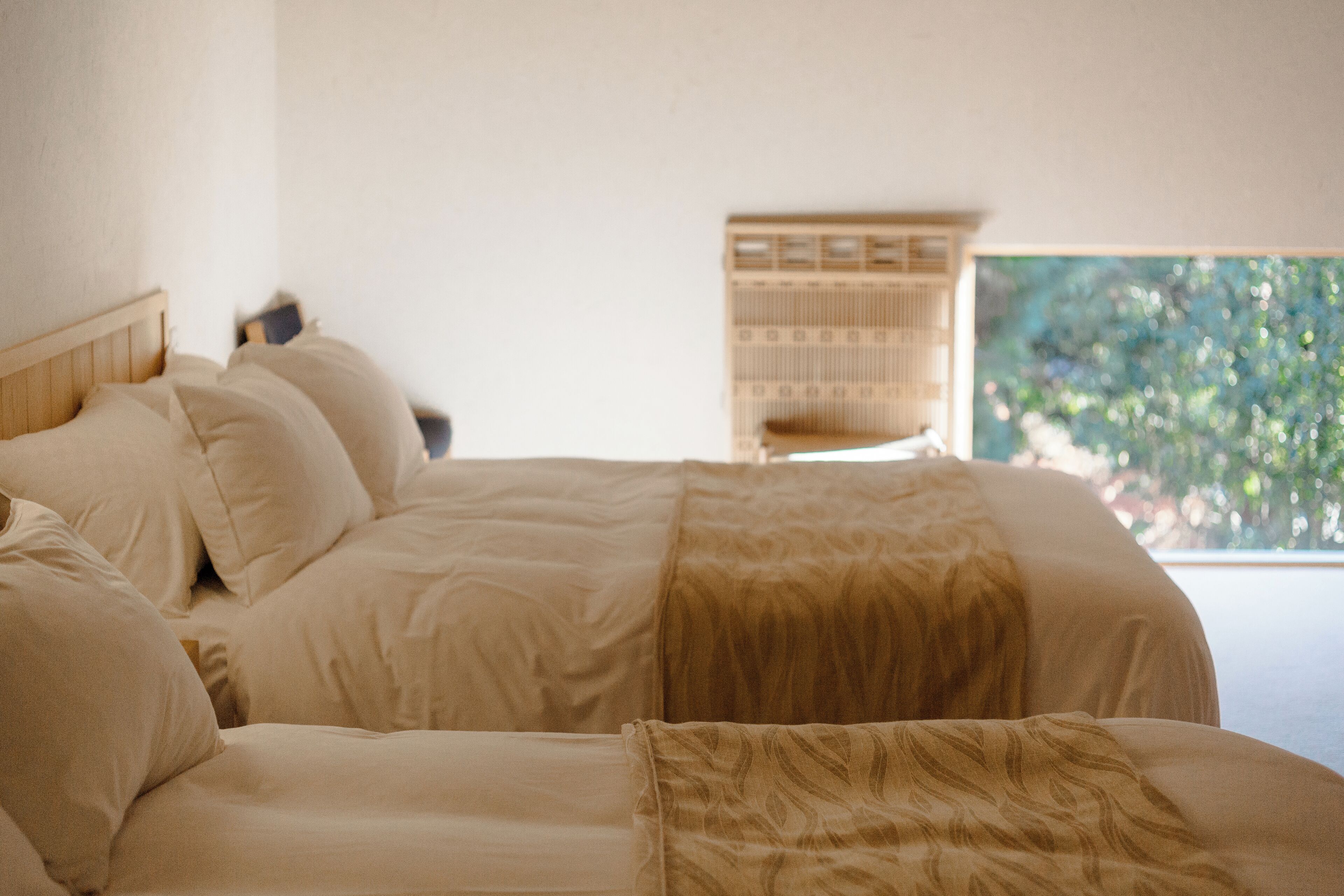 A bed with a headboard, multiple pillows, and a window with a view of greenery.