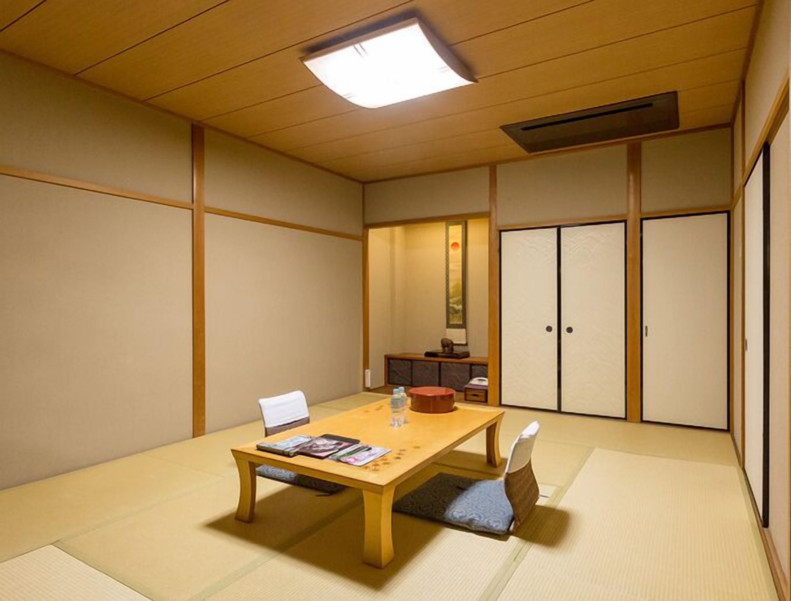 Une pièce de style japonais traditionnel, avec un sol recouvert de tatamis, une basse table en bois, une chaise blanche et des portes coulissantes.