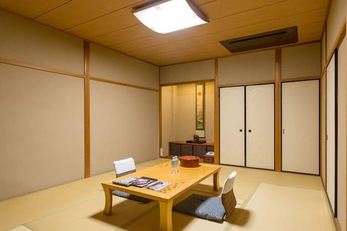 Une pièce de style japonais traditionnel, avec un sol recouvert de tatamis, une basse table en bois, une chaise blanche et des portes coulissantes.