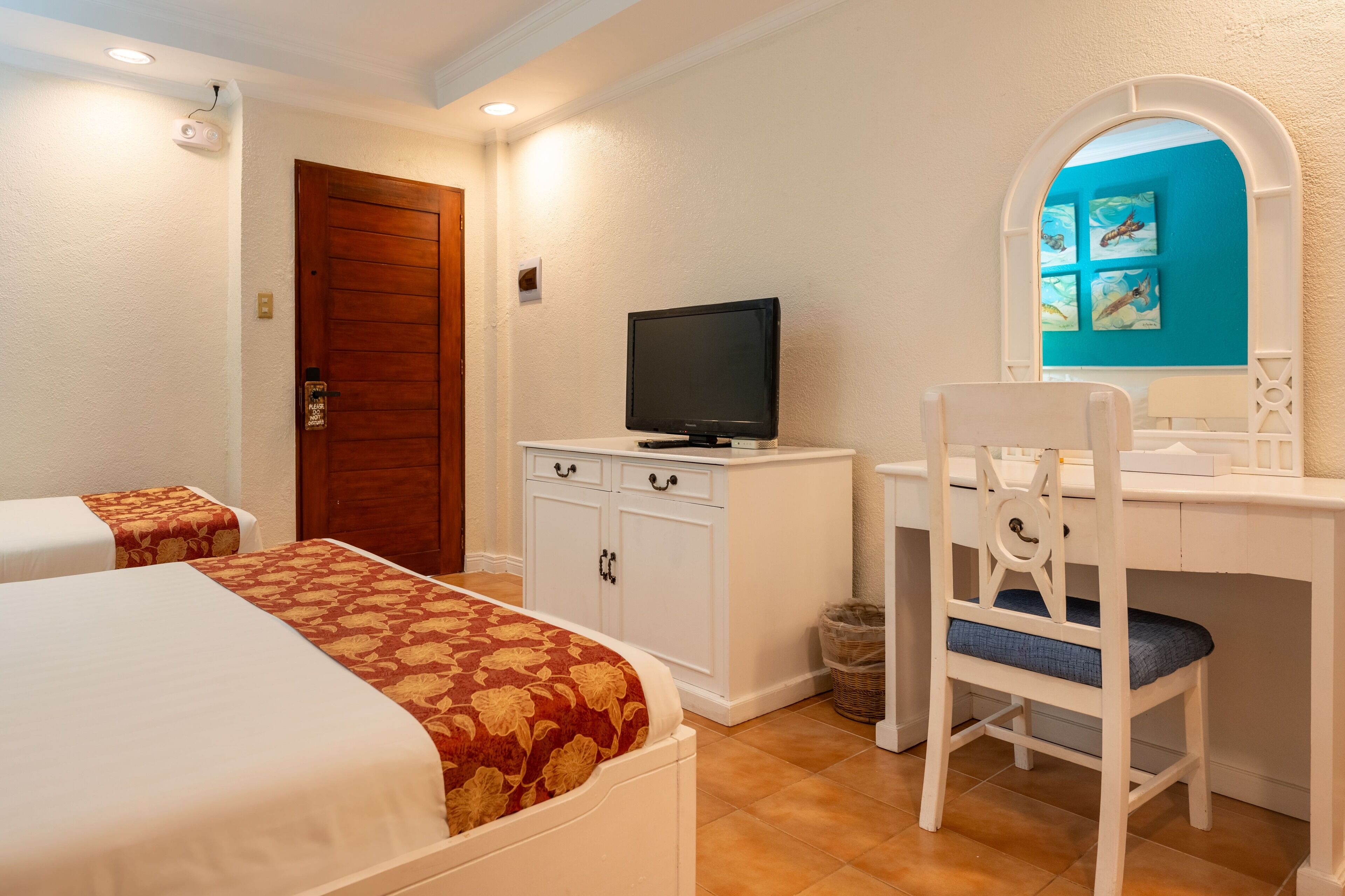 A hotel room with two beds, a TV on a white cabinet, a desk with a chair, and a bathroom door.