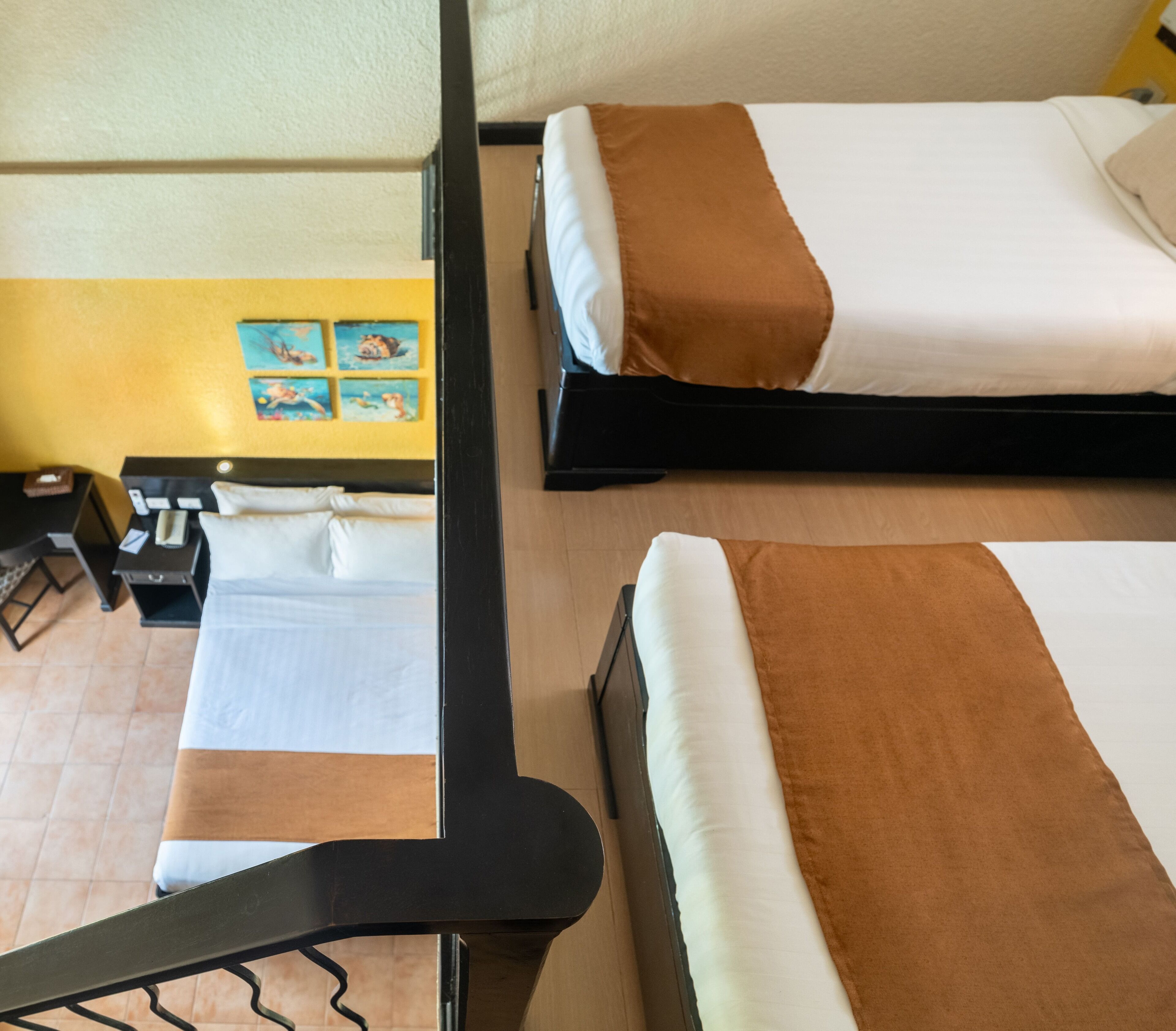 A hotel room with two beds, a desk with a chair, and a small table with a lamp.