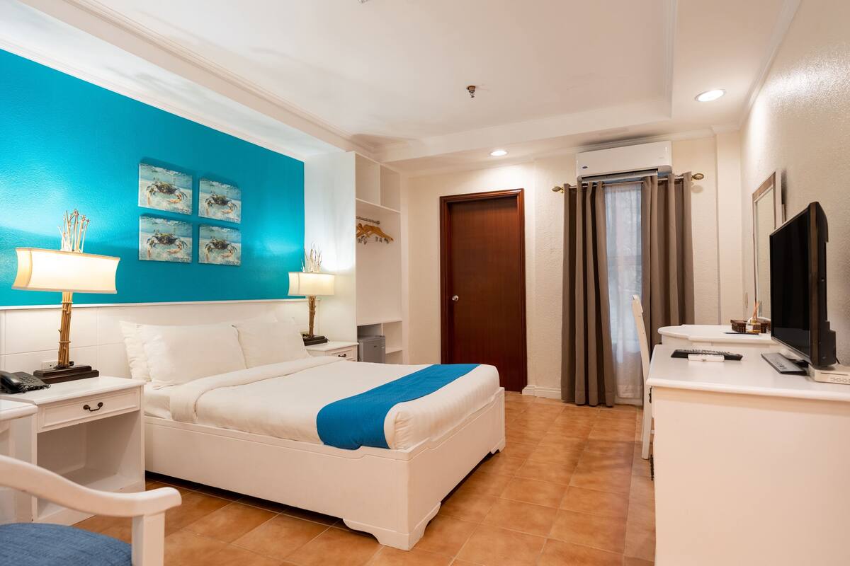 Een hotelkamer met een bed, nachtkastjes, een bureau, een stoel, een televisie en kunst aan de muur.