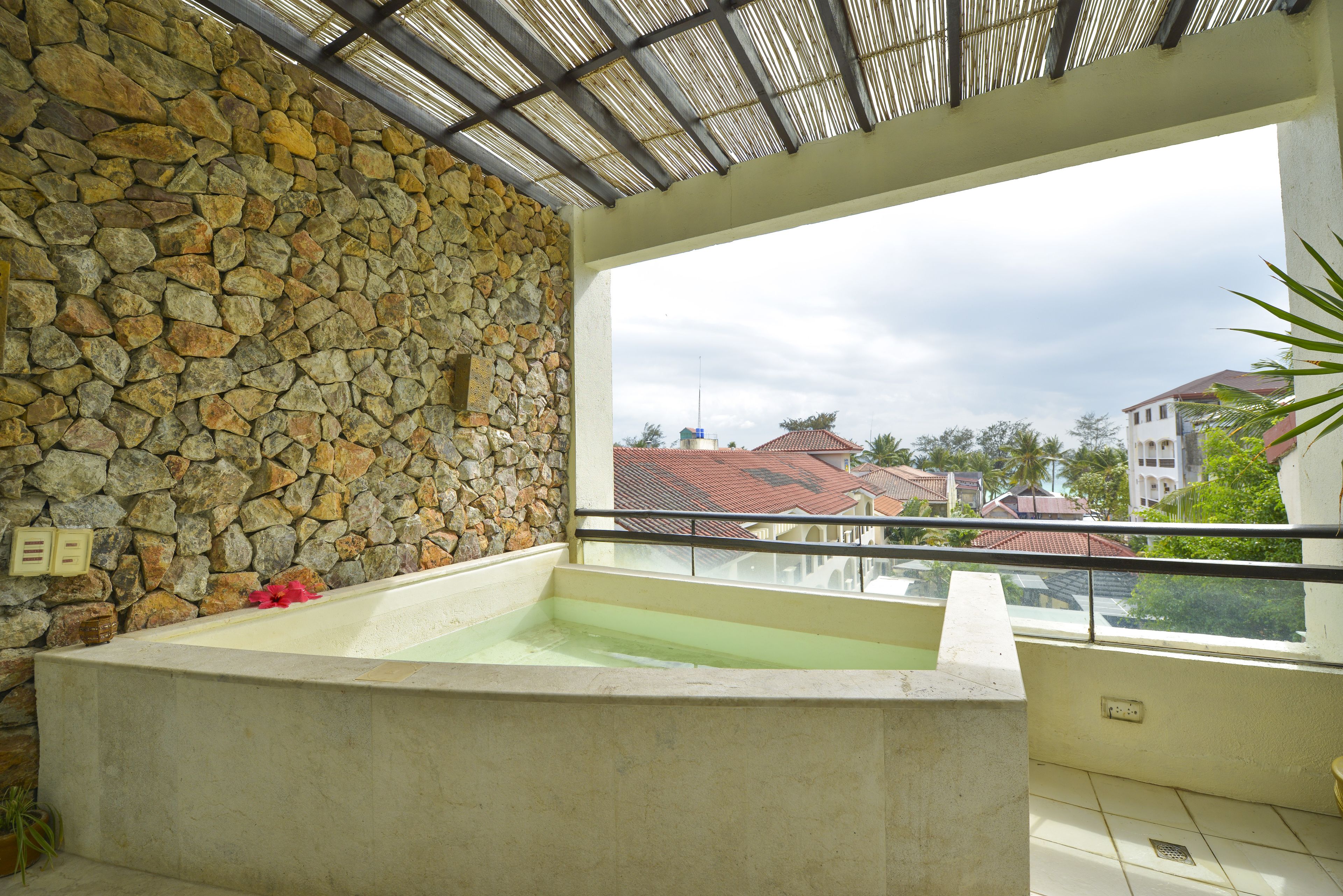 A stone wall, a bathtub, and a balcony with a view of buildings.