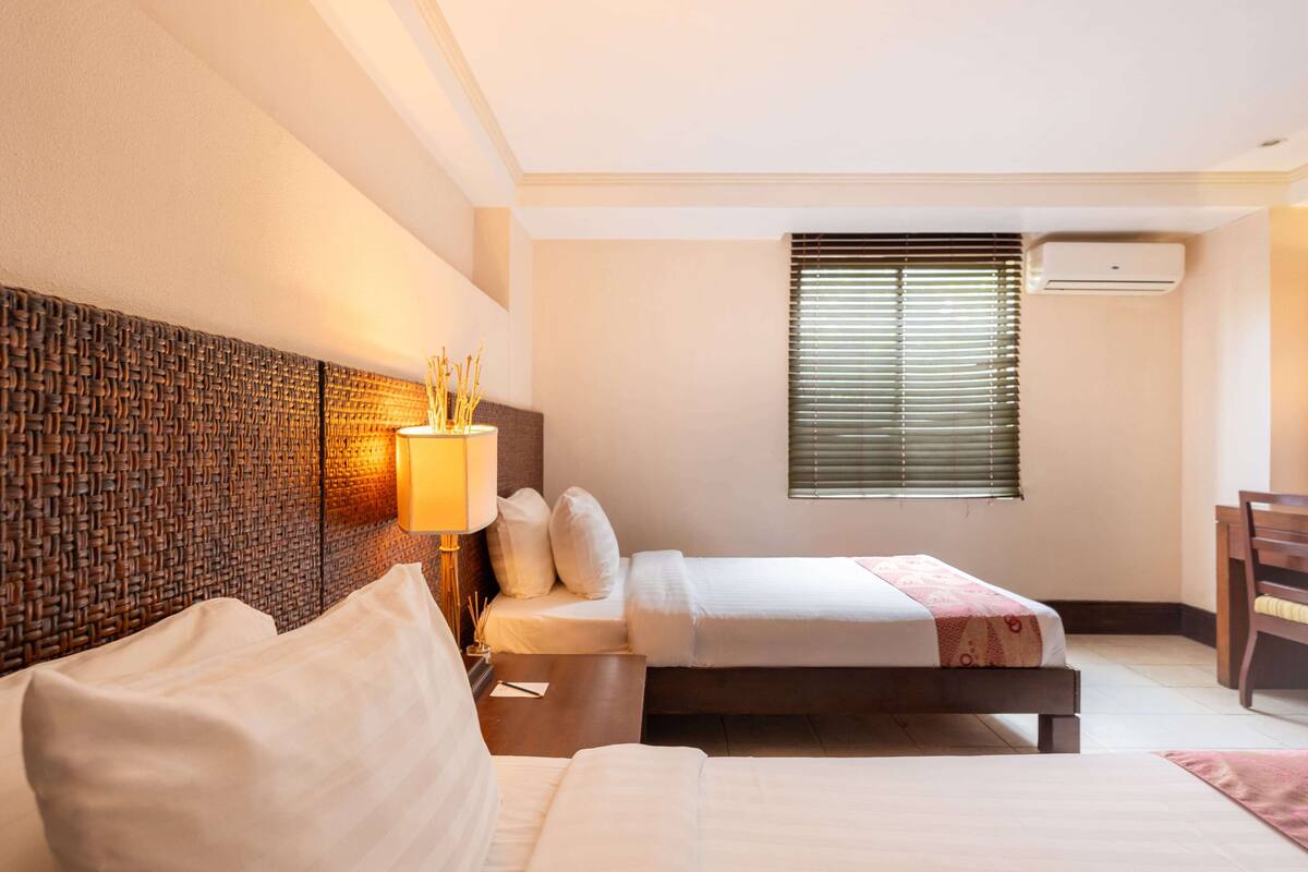 Een hotelkamer met een bed, nachtkastje, lamp en een raam met zonwering.