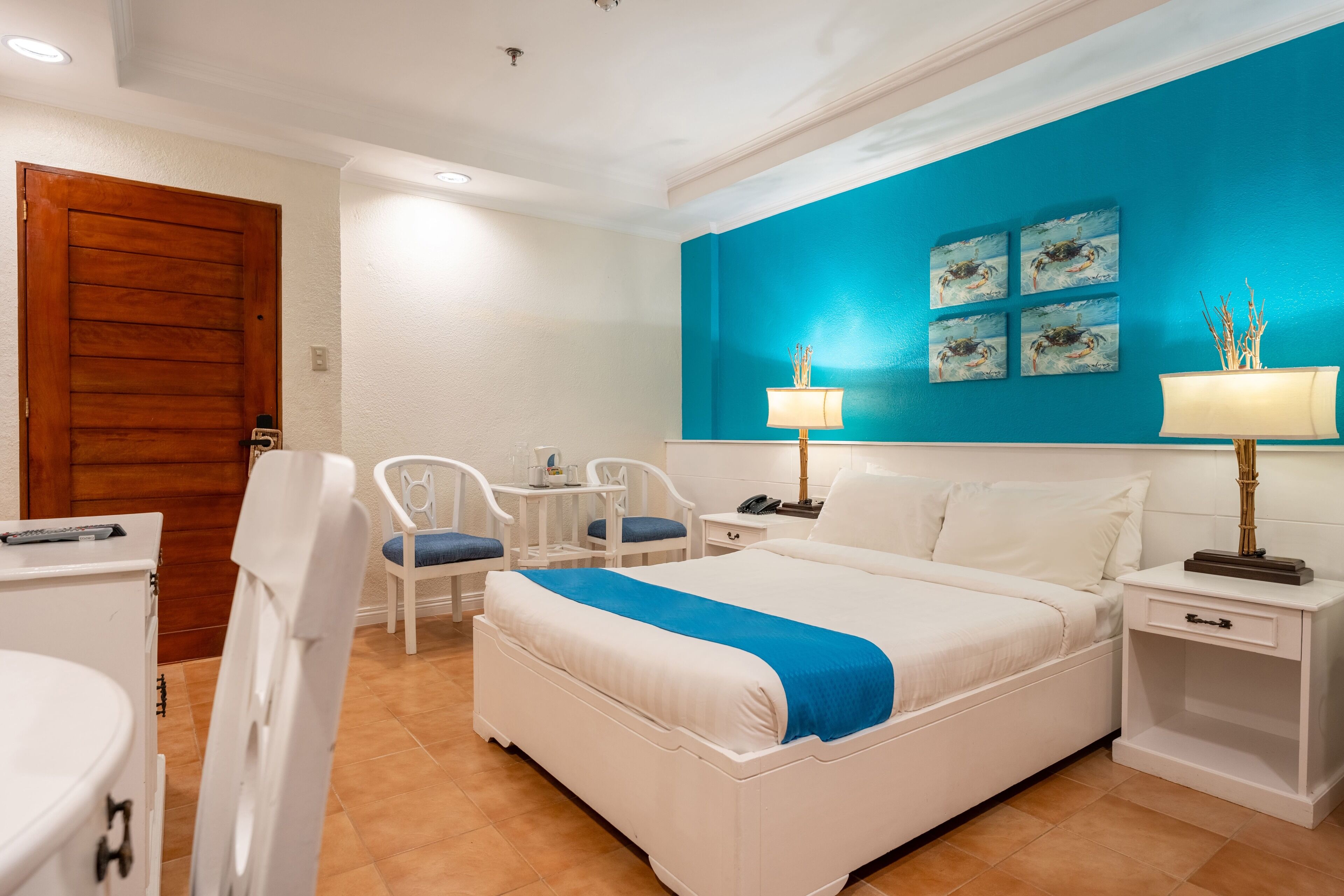 Habitación de hotel con una cama grande, un escritorio con silla, una puerta de madera y una pared azul decorativa.