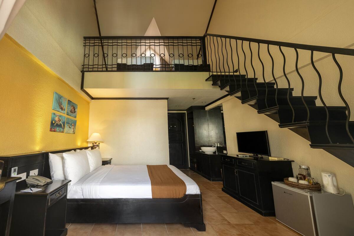 Een hotelkamer met een bed, bureau en een trap naar een hoger niveau.
