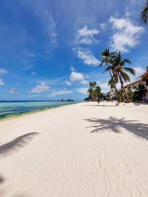 Ein Strand mit weißem Sand, Palmen und einem klaren, blauen Himmel.