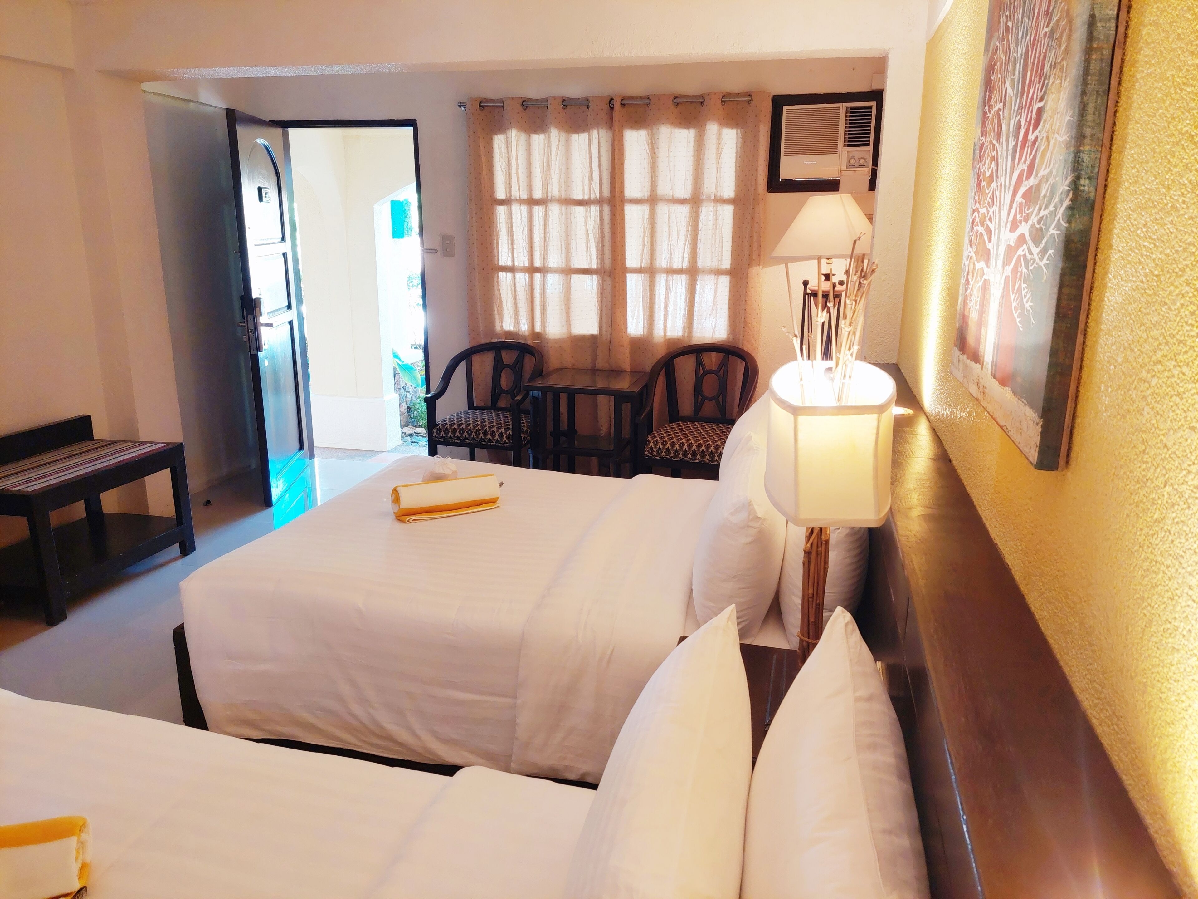 A hotel room with two beds, a desk, a chair, and a window with curtains.