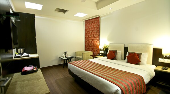 Habitación de hotel con una cama grande, televisión, escritorio con cafetera y una mesita con silla.