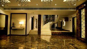 Eine geräumige Lobby mit Marmorboden, einer Treppe und einem modernen Kronleuchter.