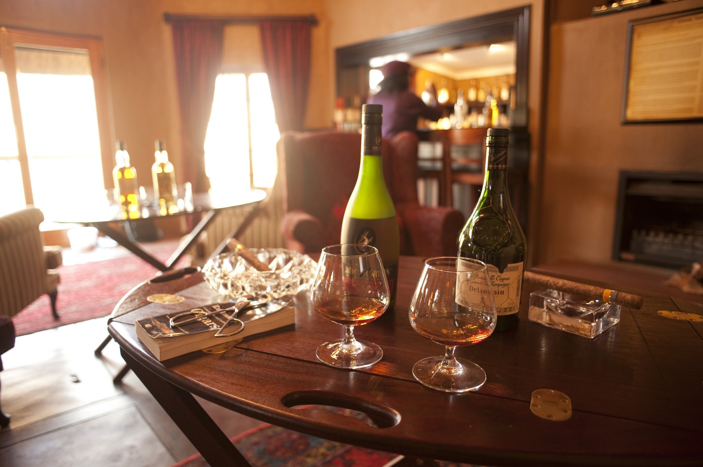 A bar area with a wooden table, glasses, a bottle of wine, and a cigar.