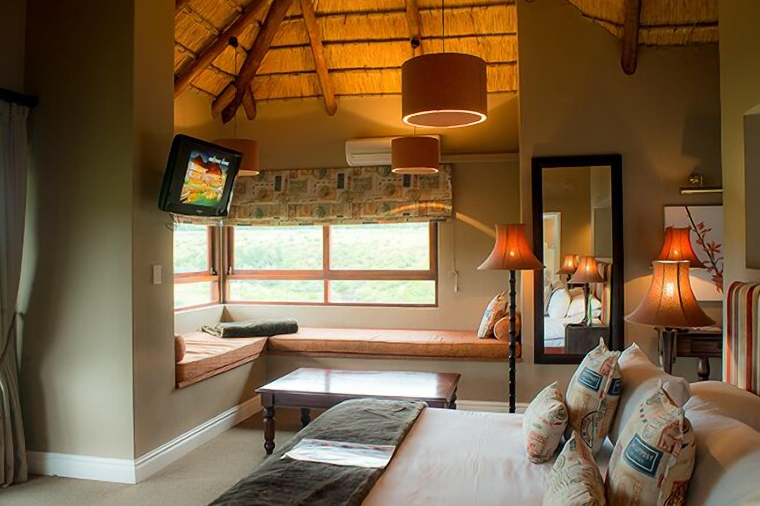 A room with a bed, a bench, a table, a TV, and a window with a view of the outdoors.