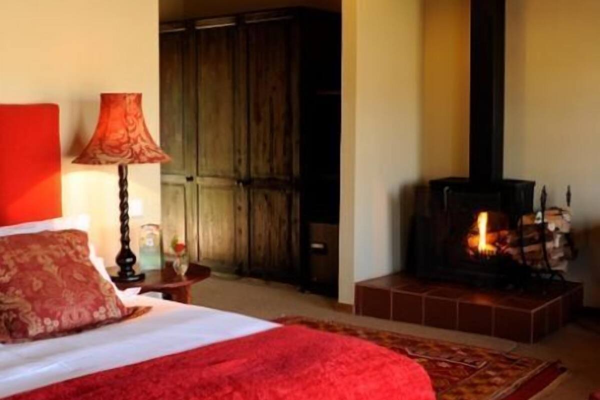 A cozy bedroom with a large bed, a wooden wardrobe, a fireplace, and a hanging light fixture.