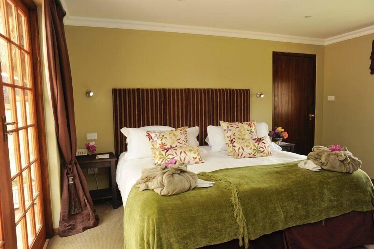 A hotel room with a large bed, a wooden headboard, a green throw blanket, and a wooden door.