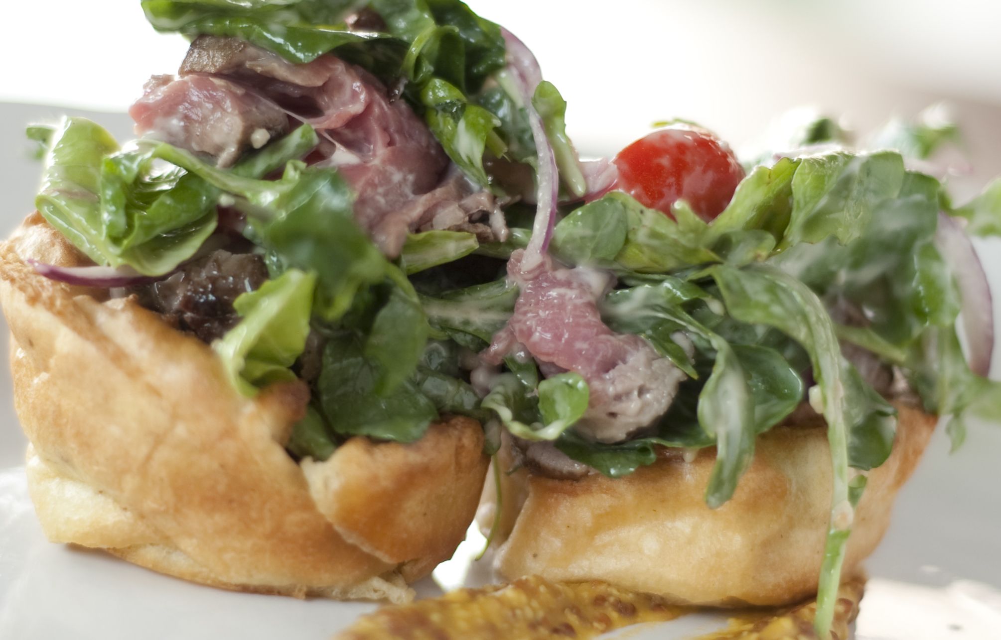 A sandwich with various greens and meats on a white plate.