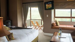 A hotel room with a bed, a television, a window seat with a view, and a table with bottles. - Granny Mouse Country House & Spa (Lidgetton West)