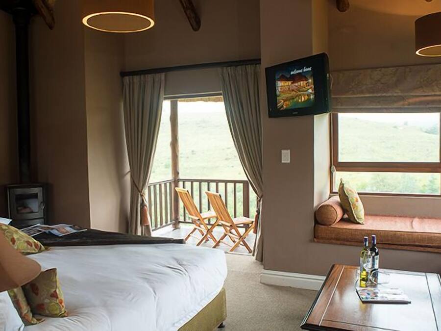 A hotel room with a bed, a television, a window seat with a view, and a table with bottles.