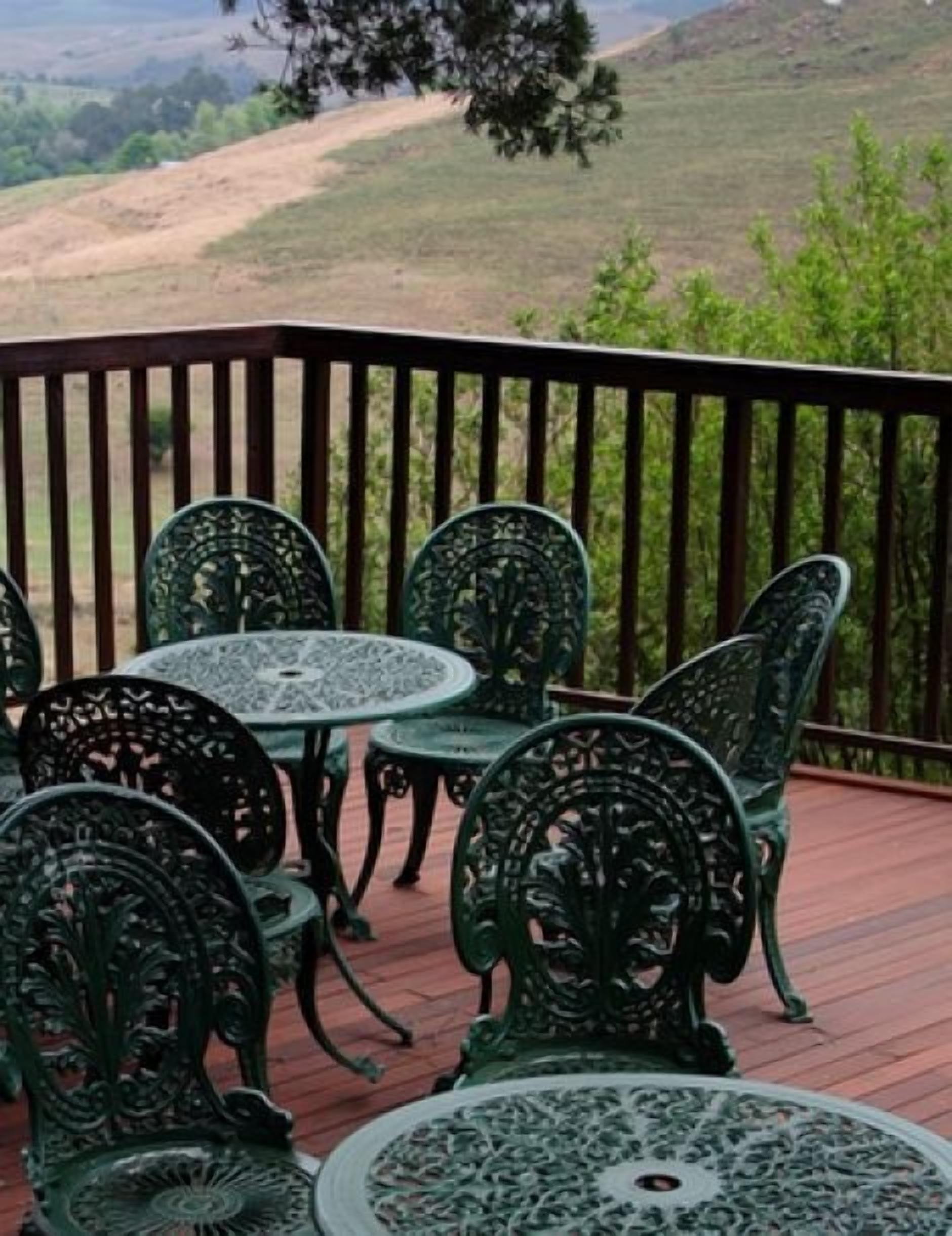Una terrazza con sedie e tavoli in metallo verde, affacciata su un paesaggio collinare.