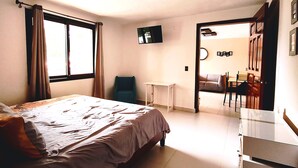 A bedroom with a bed, a TV mounted on the wall, a chair, and a small table. - Hotel Jardines del Carmen (San Cristóbal de las Casas)