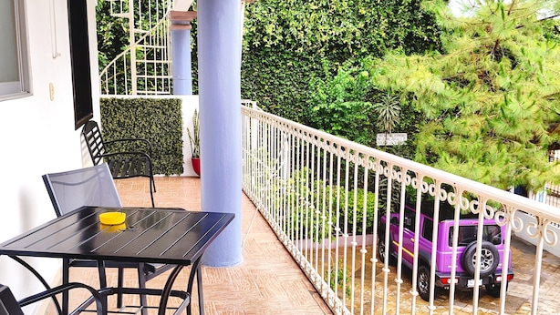 A balcony with a table and chairs, a purple SUV, and a white railing. - Hotel Jardines del Carmen (San Cristóbal de las Casas)