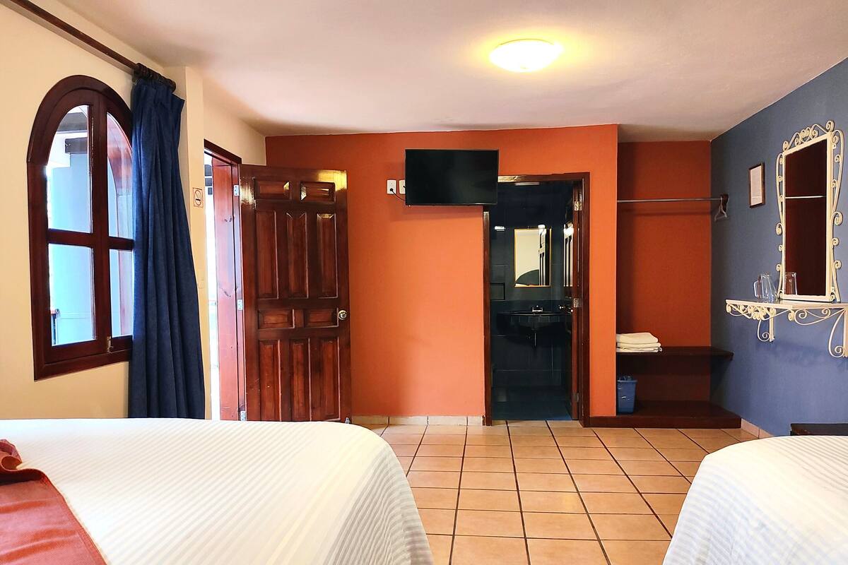 Une chambre d’hôtel avec deux lits, une salle de bain équipée d’un lavabo et d’un miroir, et un téléviseur fixé au mur.
