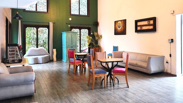 A spacious living area with a high ceiling, a dining table with chairs, a sofa, and a cabinet. - Hotel Jardines del Carmen (San Cristóbal de las Casas)