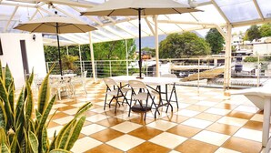 A covered patio area with checkered flooring, white tables and chairs, and large umbrellas. - Hotel Jardines del Carmen (San Cristóbal de las Casas)