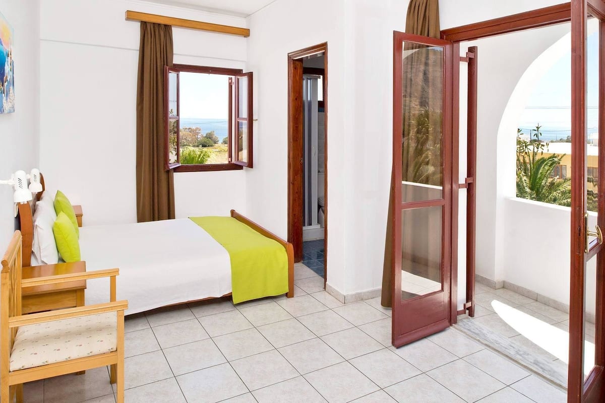 Ein Schlafzimmer mit Bett, Stuhl, Fenster mit Ausblick und einer Tür zu einem anderen Raum.