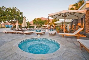A pool area with lounge chairs and umbrellas, surrounded by trees and a mountain backdrop. - Hotel Makarios (Santorini)