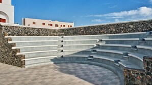A stone wall with a series of steps leading up to a white building with red windows. - Hotel Makarios (Santorini)