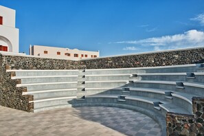 A stone wall with a series of steps leading up to a white building with red windows.