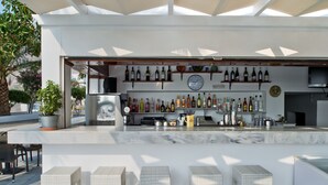 A bar area with a marble countertop, wicker bar stools, and a variety of liquor bottles. - Hotel Makarios (Santorini)