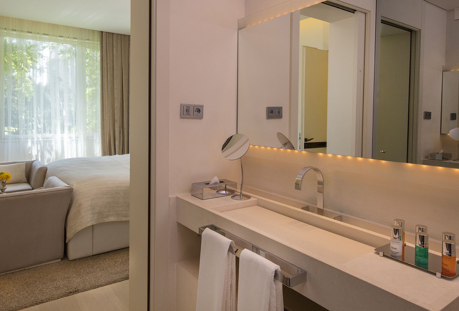 Une salle de bain d’hôtel avec un grand miroir, un lavabo et un porte-serviettes.